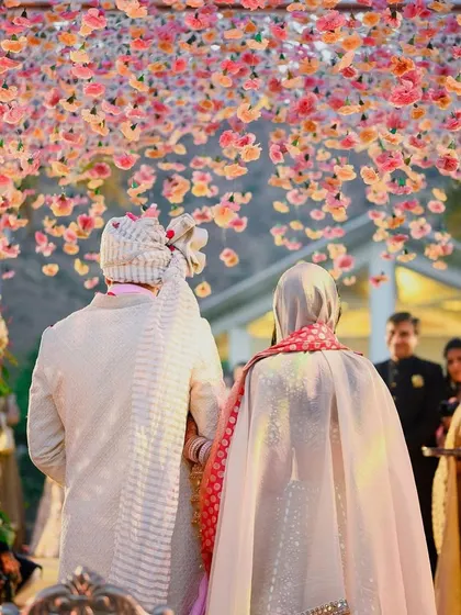 A view from behind the couple as they walk through the mandap, with a canopy of floating pink flowers creating an unforgettable moment.
