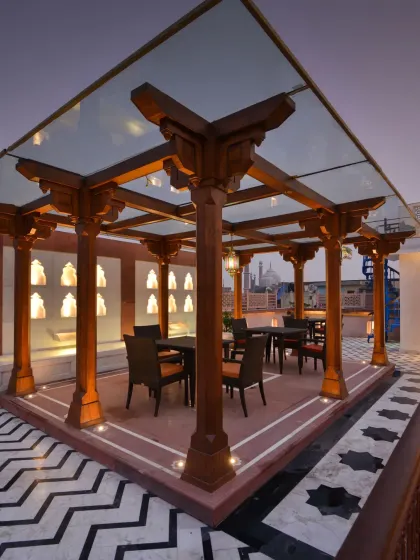 The 'Barah Dhari' on the terrace, a dining structure with wooden-clad columns and a glass pergola. The design, including the zigzag floor pattern and water wall, creates an elegant dining environment.