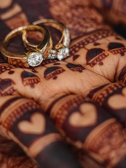 Another artistic close-up of the engagement rings on the palm. The intricate details of the henna, including the tiny hearts on the fingers, are clearly visible.