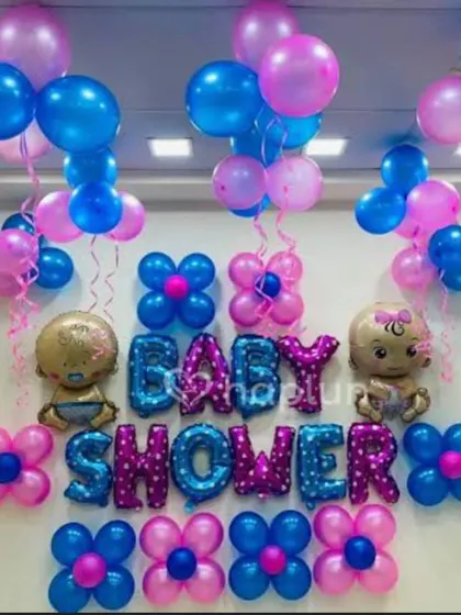 A colorful baby shower backdrop with pink and blue balloons and foil letters. The wall is decorated with flower-shaped balloon clusters.