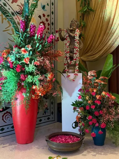 At the entrance, a statue of Krishna is flanked by vibrant floral arrangements in red and orange hues. This detail infuses the welcome with a sense of culture, craft, and devotion.