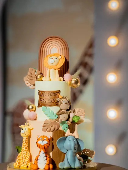 A close-up of a beautifully crafted safari-themed cake. The cake features fondant figures of a lion, tiger, elephant, and giraffe.