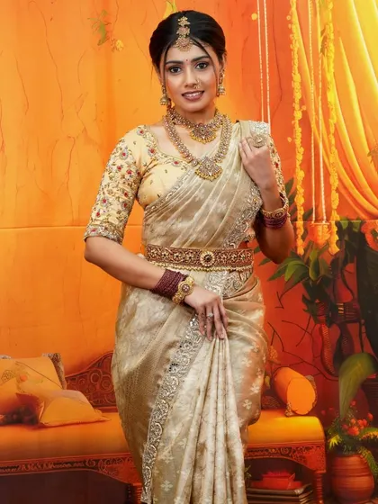 The epitome of grace, this cream and gold silk saree is for those who love understated elegance. It's a versatile piece, perfect for housewarming ceremonies, engagement parties, or as a guest at a wedding, offering a classic and sophisticated look.