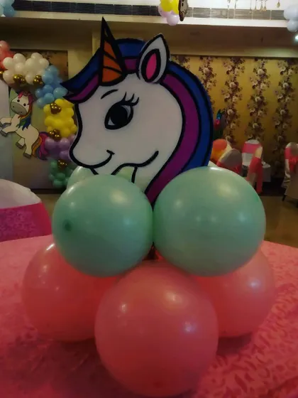A simple yet adorable unicorn-themed centerpiece for a table, featuring a unicorn head cutout on a base of green and pink balloons.