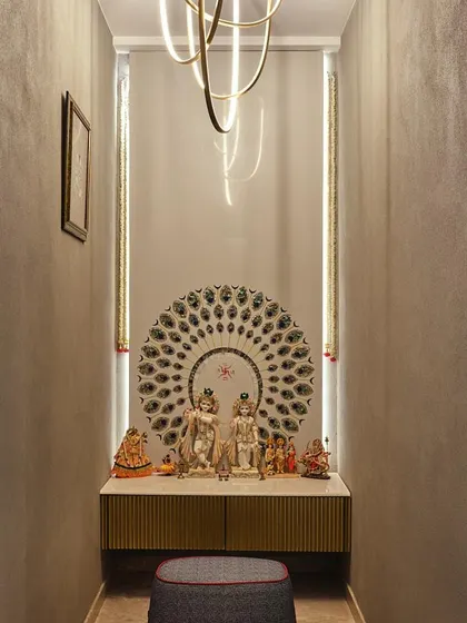 A compact and elegant pooja space featuring a marble platform, a peacock-feather-inspired backdrop, and warm vertical lighting. This design shows how a serene prayer corner can be created even in a smaller area.