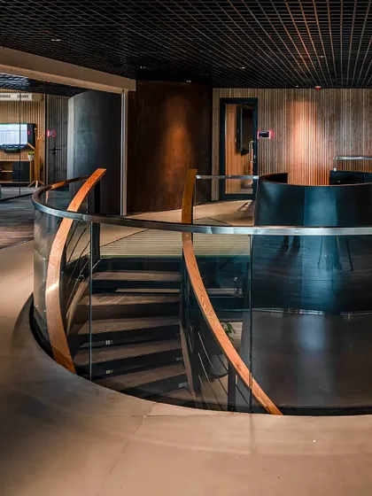 The curved glass balustrade of the central staircase at BCG HQ reflects the surrounding wood and metal textures, creating a sense of continuous, flowing movement.