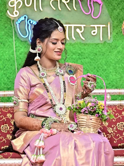 A candid shot capturing a quiet moment during the baby shower festivities. The client is adorned in a beautiful lilac saree and custom floral jewelry, with makeup that highlights her gentle smile.