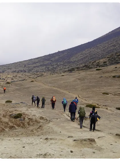 A group of trekkers ascending a wide, open trail in the higher reaches of the Khumbu. The landscape becomes more barren and dramatic as you gain altitude.