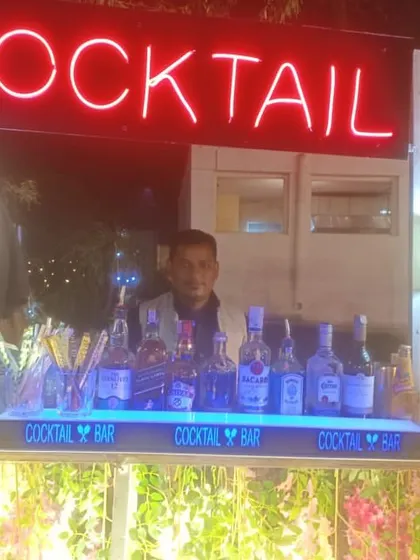 Our bartender posing at a floral-decorated cocktail bar, ready for a daytime wedding event.