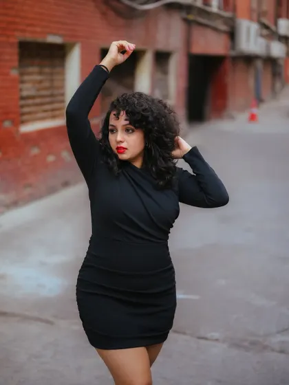 A dynamic portrait of a model in a black dress against a gritty urban alley. Her pose and the setting create a powerful and expressive fashion image.