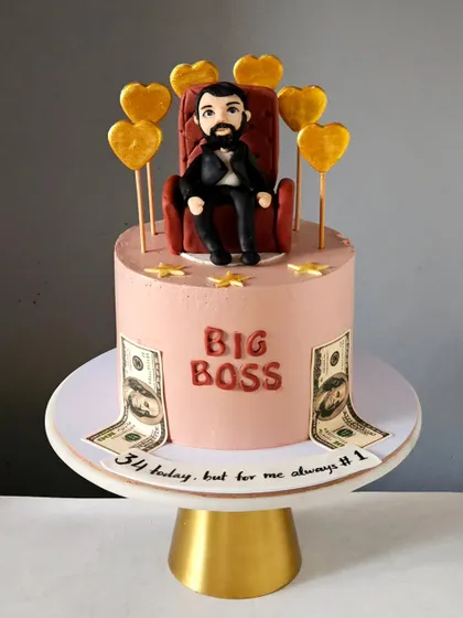 A fun "Big Boss" themed cake for a husband's birthday. The centerpiece is a handmade figurine sitting on a throne, surrounded by edible money and golden hearts, making for a playful and celebratory design.