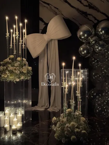 A close-up of the glamorous black and white decor, focusing on the oversized bow, candelabras, and white floral arrangements on acrylic stands.