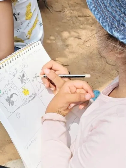 A child carefully documents their findings in a nature journal during a "square foot of soil" observation activity.