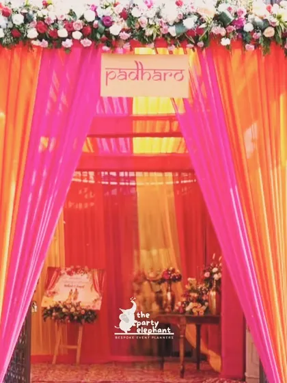 The entrance to the Haldi and Mehendi ceremony was a vibrant tunnel of pink and orange drapes, topped with a floral border and a 'Padharo' sign to welcome guests in traditional style.