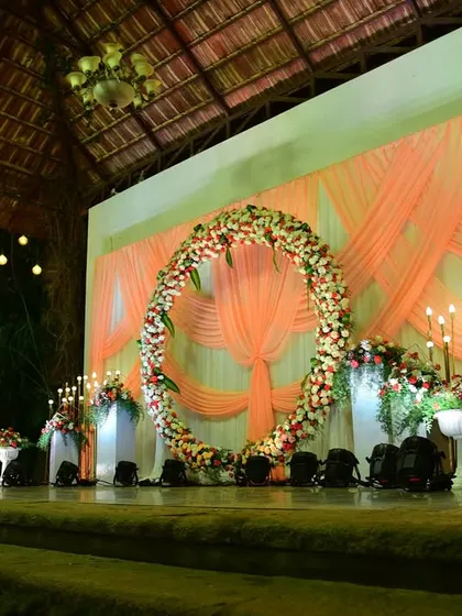 A beautiful engagement stage with a full floral ring and peach-colored drapes, set in a rustic, open-air venue.