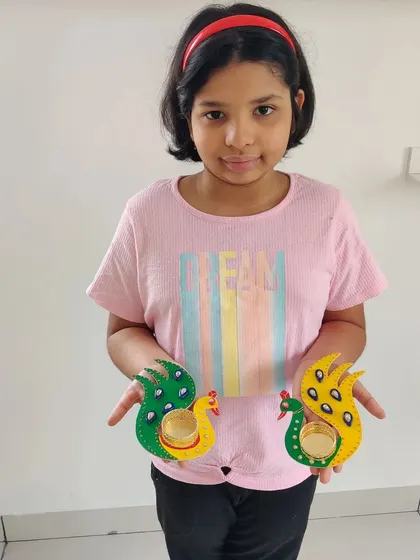 So much pride in her finished work! She made this pair of bright and colorful peacock T-light holders herself, and they are ready to light up her home for Diwali.