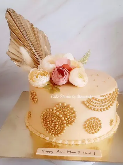 A stunning anniversary cake made completely without fondant. The design features intricate golden beadwork inspired by henna art, topped with flowers and a dried palm spear.