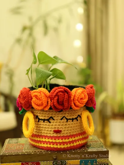 The Frida Basket, shown here holding a lush green plant. The contrast between the vibrant crochet and the natural plant is just lovely.