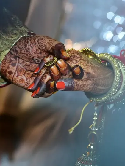 A macro shot of the couple holding hands during a wedding ritual, emphasizing their connection and the intricate details of their attire and mehendi.