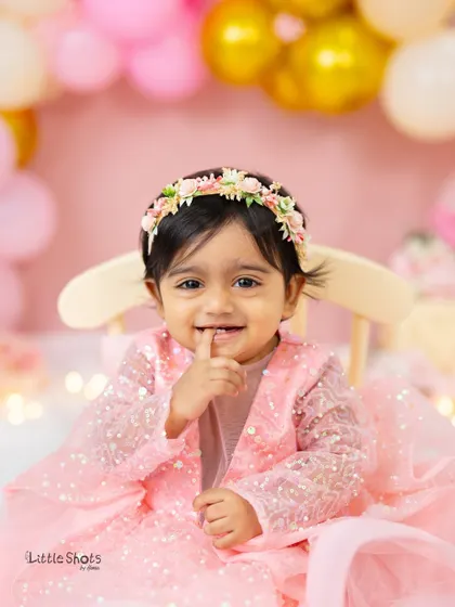 A close-up of the birthday girl's sweet, shy smile. Her adorable expression and sparkly pink dress make this first birthday portrait extra special.