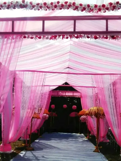 A fully draped entrance passage for a wedding or reception. The structure is covered in bright pink fabric with crystal strings hanging down, creating an elegant and colorful welcome.