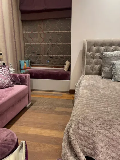 This shot highlights the cozy window seat, a perfect reading nook. The combination of the plush purple upholstery and the textured roman blinds adds another layer of comfort and style to the room.