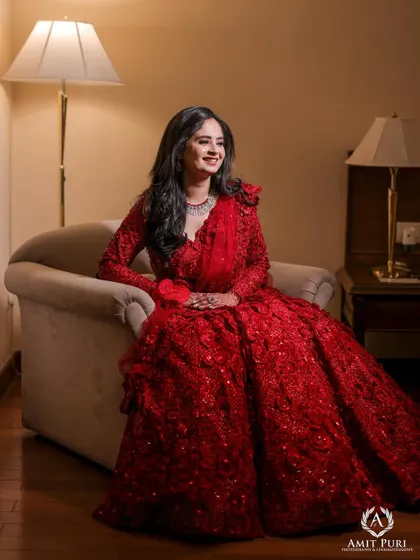An elegant bridal portrait, seated in a comfortable armchair. The soft lighting and her relaxed pose create a look of effortless grace in her beautiful red reception gown.