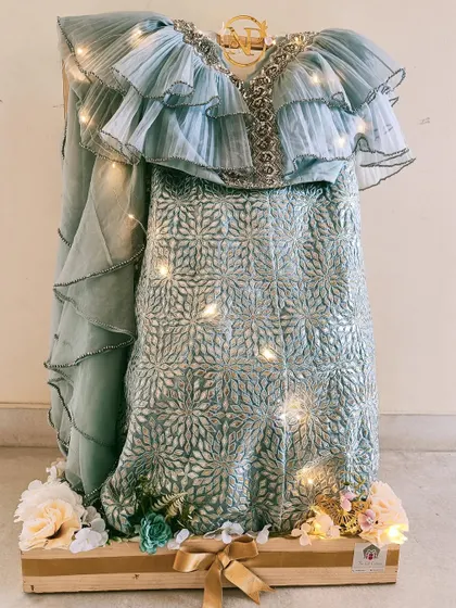 A close-up of a designer lehenga displayed on a custom stand. The fairy lights woven into the display add a magical sparkle to the intricate outfit.