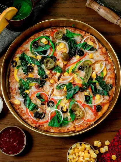 A vibrant, fully loaded vegetable pizza presented in a brass pan. The top-down angle showcases the colorful toppings like bell peppers, olives, and corn, making it look fresh and irresistible.