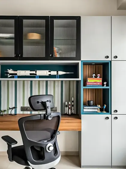 We designed this integrated study area to be both stylish and productive. The setup includes a mix of open and closed overhead storage, with fluted glass doors and dedicated display nooks for personal items, all built around a spacious wooden desk.