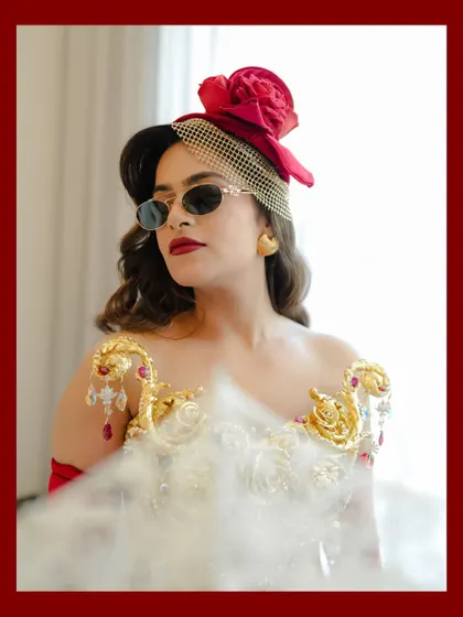 A portrait of rebellious glamour. The sunglasses, the red fascinator, and the confident pose all tell a story of a bride with a strong personal style.