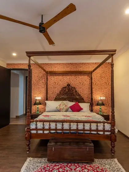 A luxurious master bedroom with a classic four-poster bed set against a dusty orange accent wall. The design includes a walk-in closet area separated by stylish green doors.