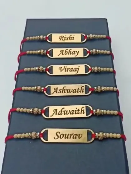 A collection of metal name rakhis with beaded threads, displayed in a gift box.