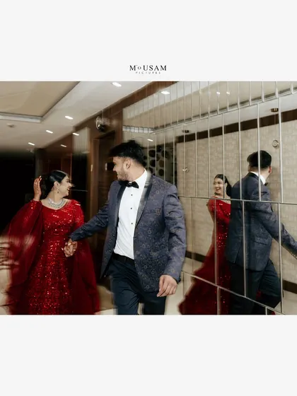 The couple makes a grand entrance at their reception. The groom leads his bride, who is stunning in a red gown, through a hall of mirrors, creating a dynamic and glamorous shot.