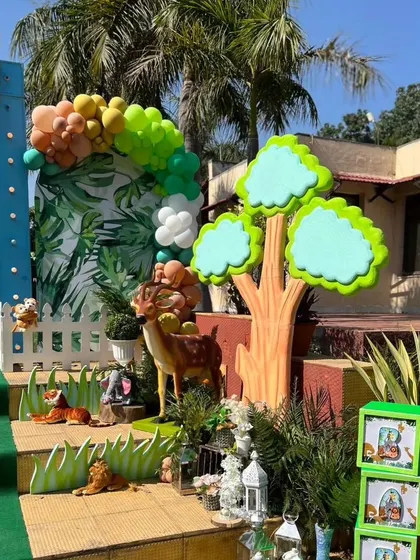 A detailed photo spot for a jungle party, with a deer, a tree cutout, and a white picket fence against a leafy backdrop.