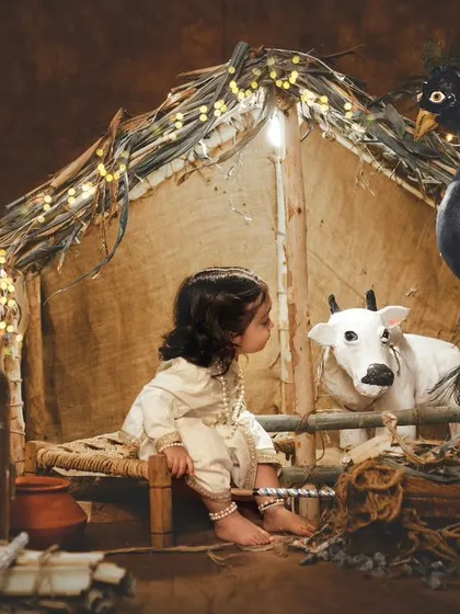 A quiet, contemplative moment between our little Krishna and the cow prop, with the warm glow of the hut behind them.