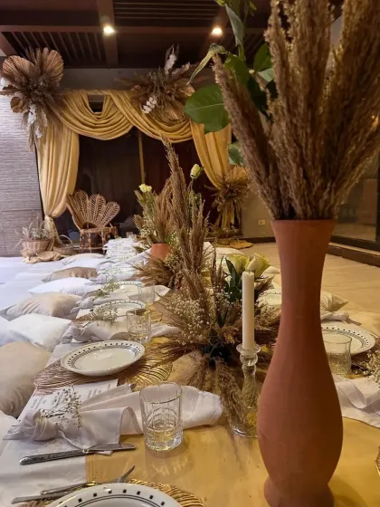 A close-up of the tablescape for the themed dinner. Terracotta vases with dried wheat, simple white plates, and candlelight create a rustic yet elegant look.