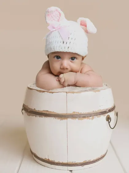 A minimalist portrait of a baby in a bunny hat, peeking over a rustic white barrel. This shows how a simple prop can create a very cute and memorable photo.