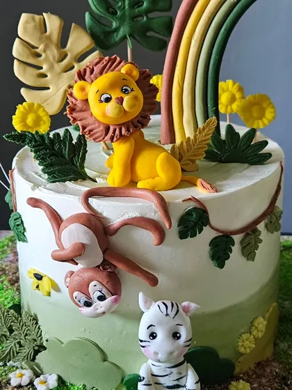 A close-up of one of the jungle-themed twin cakes. This view highlights the adorable, hand-sculpted lion, monkey, and zebra figurines.