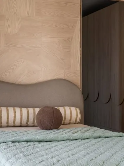 A close-up of the bed in the Aikaa villa, highlighting the gentle curves of the headboard and the beautiful grain of the wood-paneled wall. It’s all about creating a calm, tactile experience.