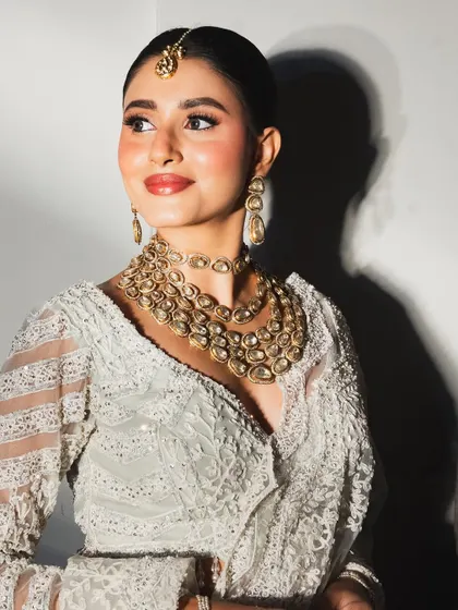A stunning bridal portrait showcasing a dewy base, warm-toned eyeshadow, and a classic red lip that perfectly complements the intricate white and gold bridal attire.