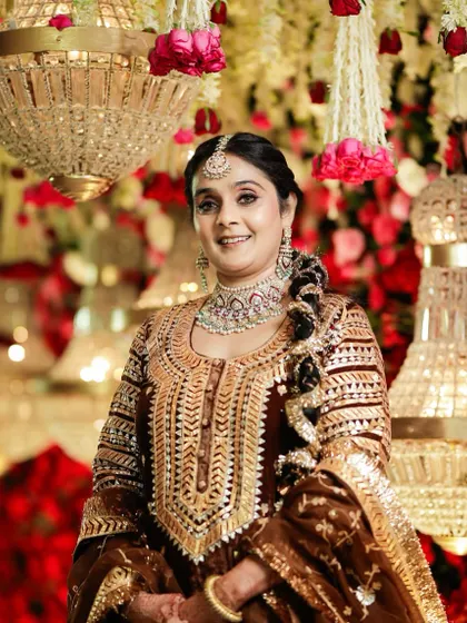 A smiling portrait against a backdrop of flowers. The makeup is designed to be visible and elegant, perfect for family members at a grand wedding.