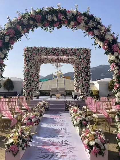 A grand floral archway leading to the wedding mandap. The path is decorated with a custom-printed aisle runner, creating a beautiful walkway for the bride.
