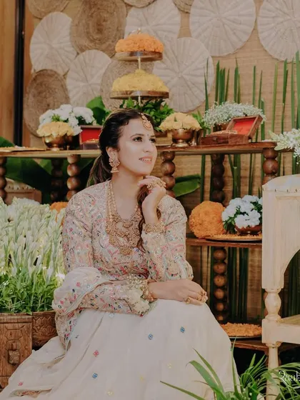 A seated portrait showing off her full look. The makeup is elegant and complements her colorful, embroidered outfit.