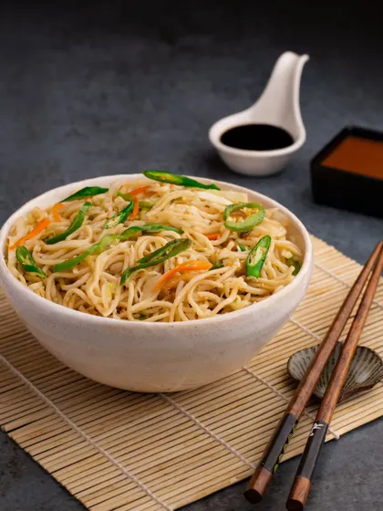 A simple bowl of chilli garlic noodles, styled to look clean and appetizing. The chopsticks and sauces in the background provide context and complete the Asian dining experience.