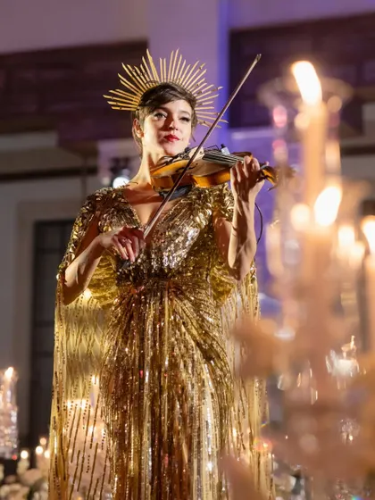 A violinist in a stunning golden gown serenades guests, adding a touch of live, ethereal music to the elegant dinner.