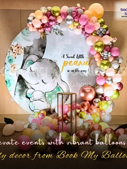 "A sweet little peanut is on the way." This adorable elephant themed baby shower decor featured a beautiful illustration on a circular backdrop, surrounded by a garland of pink, green, and chrome gold balloons.