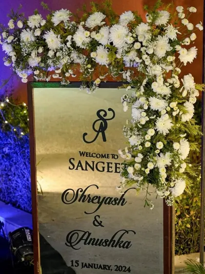 A personalized welcome sign for a Sangeet night, framed with beautiful white flowers. The elegant calligraphy and custom details make guests feel special.