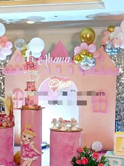 A princess castle theme for a first birthday, featuring a large pink castle backdrop, silver sequin panels, and the baby's name "Aliana" at the top.