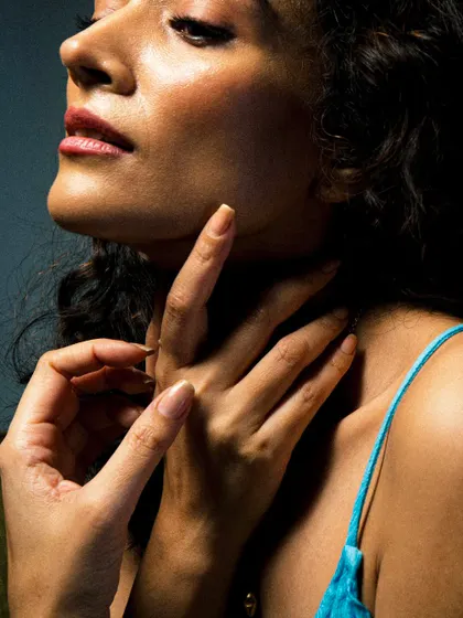 A close-up portrait focusing on texture and form. The soft light caresses the subject's skin, highlighting the elegant lines of her neck and hands in a moment of quiet grace.